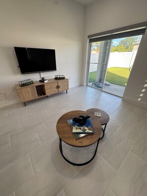 A modern living room with a flat-screen TV, wooden furniture, and a view through a glass door. - Spacious Home Near Disney & Downtown Kissimmee (Kissimmee)