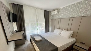 A hotel room with a bed, a bedside table, a TV mounted on the wall, and a window with curtains. - Hotel Cosmos (Ruse)