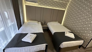 A hotel room with two single beds, a window, an air conditioning unit, and a patterned wall. - Hotel Cosmos (Ruse)