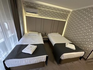 Habitación de hotel con dos camas individuales, una ventana, un equipo de aire acondicionado y una pared con diseño.