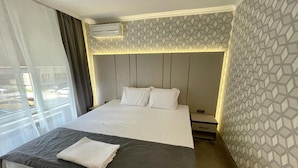 A hotel room with a large bed, a bedside table, an air conditioning unit, and a window with curtains. - Hotel Cosmos (Ruse)