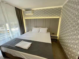 A hotel room with a large bed, a bedside table, an air conditioning unit, and a window with curtains.