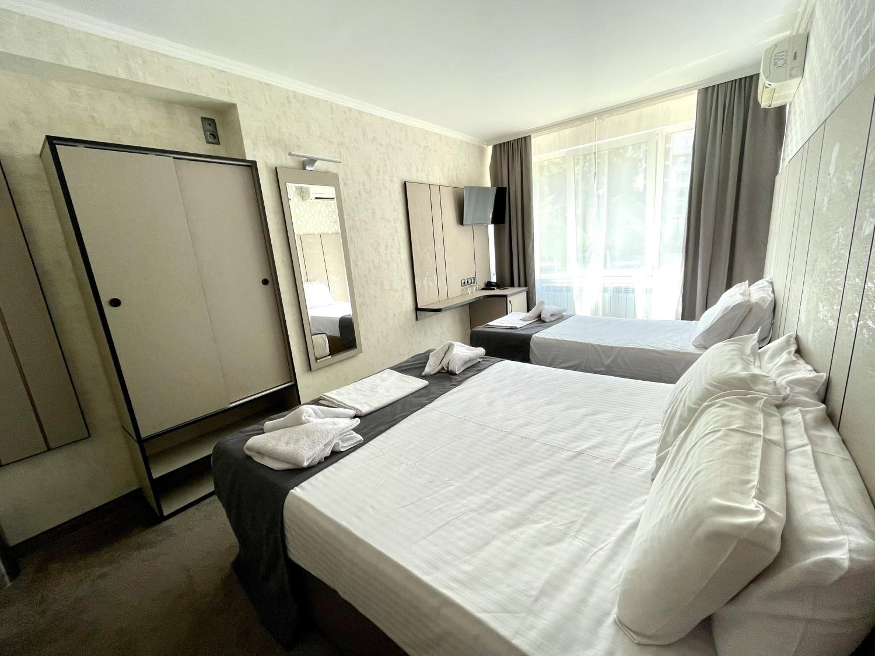 A hotel room with two beds, a wardrobe, a mirror, a television, and a window with curtains.