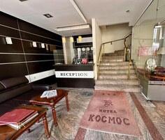 Zona de recepción de un hotel con mostrador, un sofá, una mesa de centro y una escalera que conduce al piso superior.
