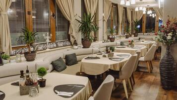 Un restaurante con una zona de asientos larga y curvada, varias mesas y plantas en macetas.