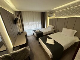 A hotel room with two beds, a desk, a chair, and an air conditioning unit.