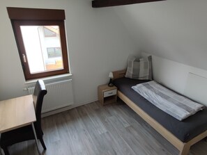 Ein Schlafzimmer mit einem Bett, einem Schreibtisch, einem Sessel, einem Nachttisch und einem Fenster.