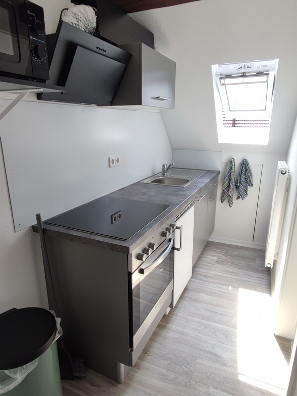 A compact kitchen with a stove, sink, and a window above the sink.