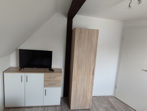 A room with a sloped ceiling, a television on a cabinet, and a large wooden wardrobe.