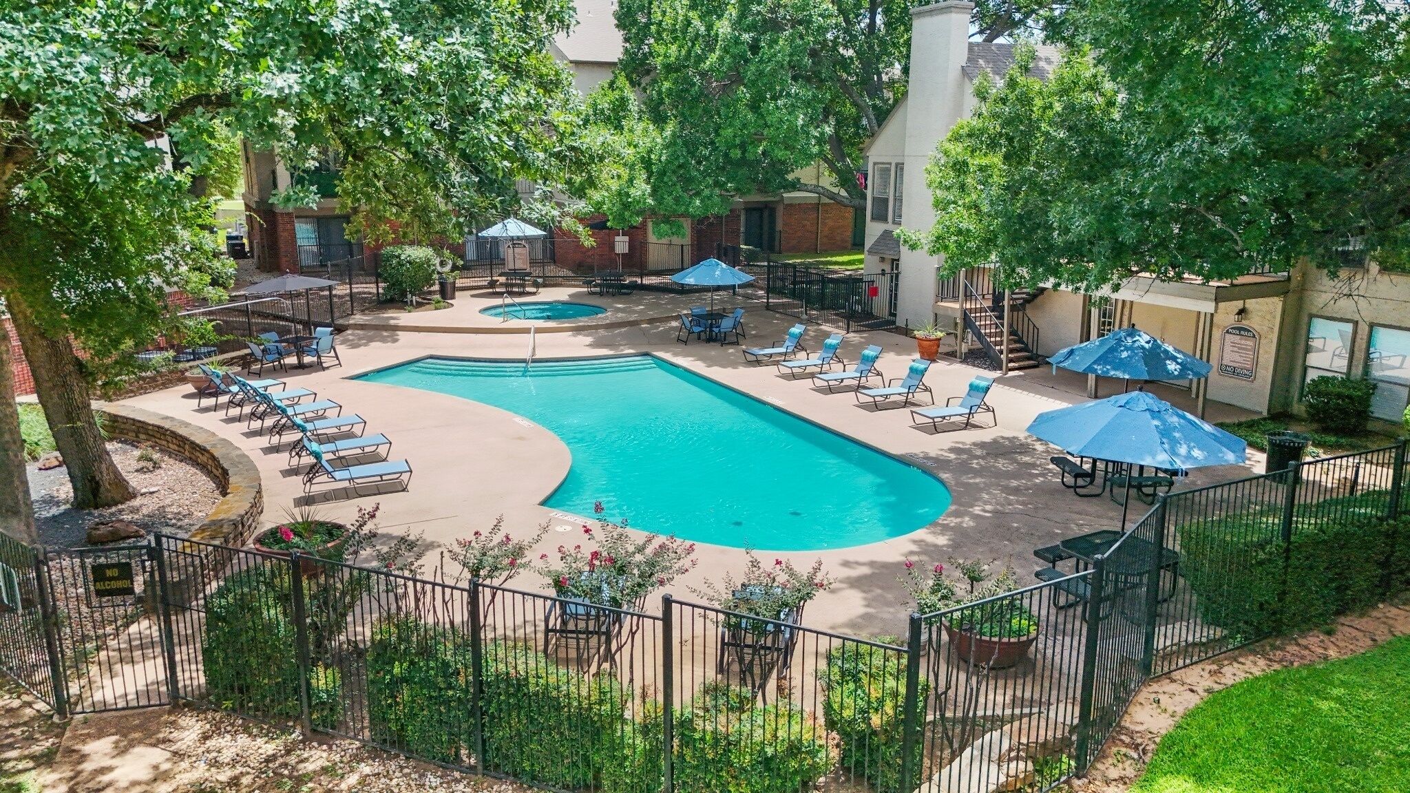 A pool area with lounge chairs and umbrellas, surrounded by trees and a fence.