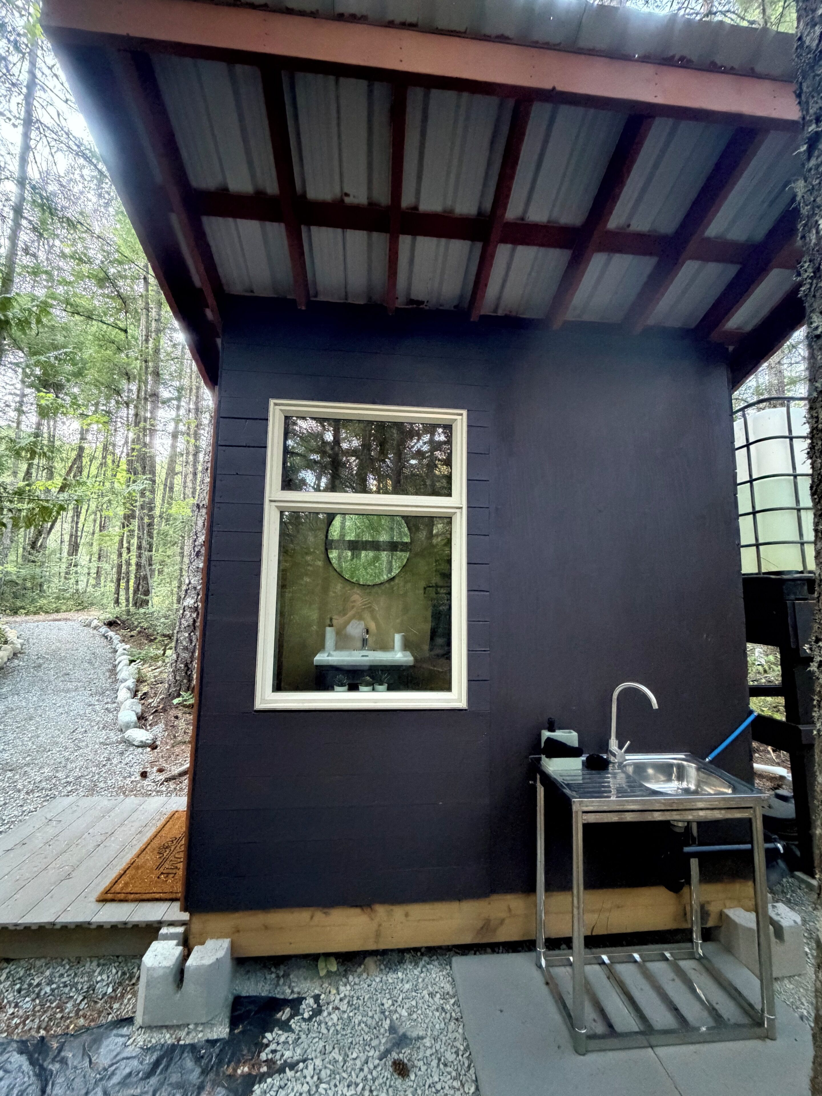 Une petite cabane de couleur sombre, dotée d’une fenêtre, d’un évier et d’une table en bois.