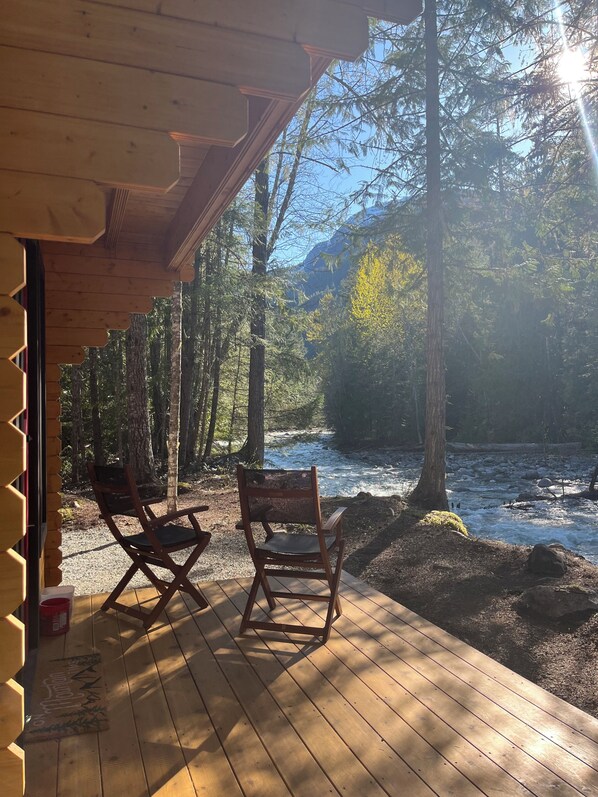 A wooden deck with two rocking chairs overlooking a river and forest.