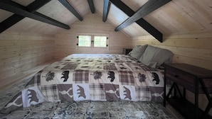 A bedroom with a wooden ceiling, a bed with a patterned bedspread, a nightstand, and a window.