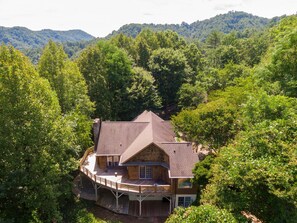 A wooden cabin with a deck, surrounded by dense forest and hills. - Hidden Falls Retreat: Private, Blowing Rock, Hot Tub (Lenoir)
