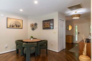 A dining area with a round table and four chairs, a ceiling light, and wall-mounted artwork.