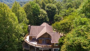 A wooden cabin with a deck, surrounded by dense forest and hills. - Hidden Falls | Private, Near Blowing Rock , Hot tub (Lenoir)