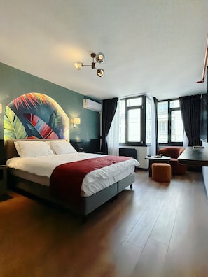 Habitación de hotel moderna con una cama grande, un escritorio, una silla y vistas a la ciudad a través de amplios ventanales.