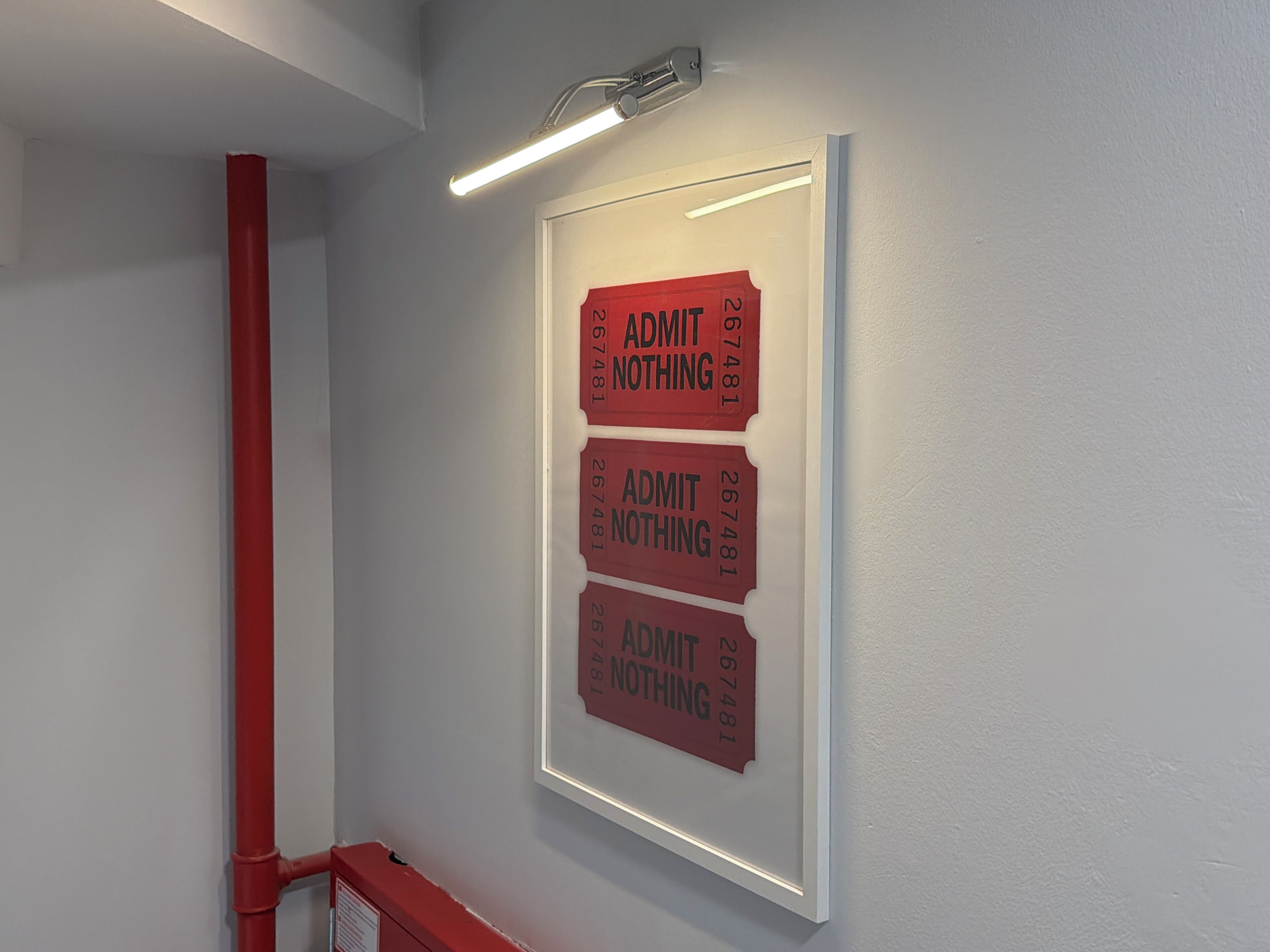 A wall with three red signs that read 'ADMIT NOTHING' and a red pipe.