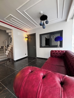 Un interior moderno con un sofá rojo, una escalera, un espejo con marco negro y una lámpara roja.