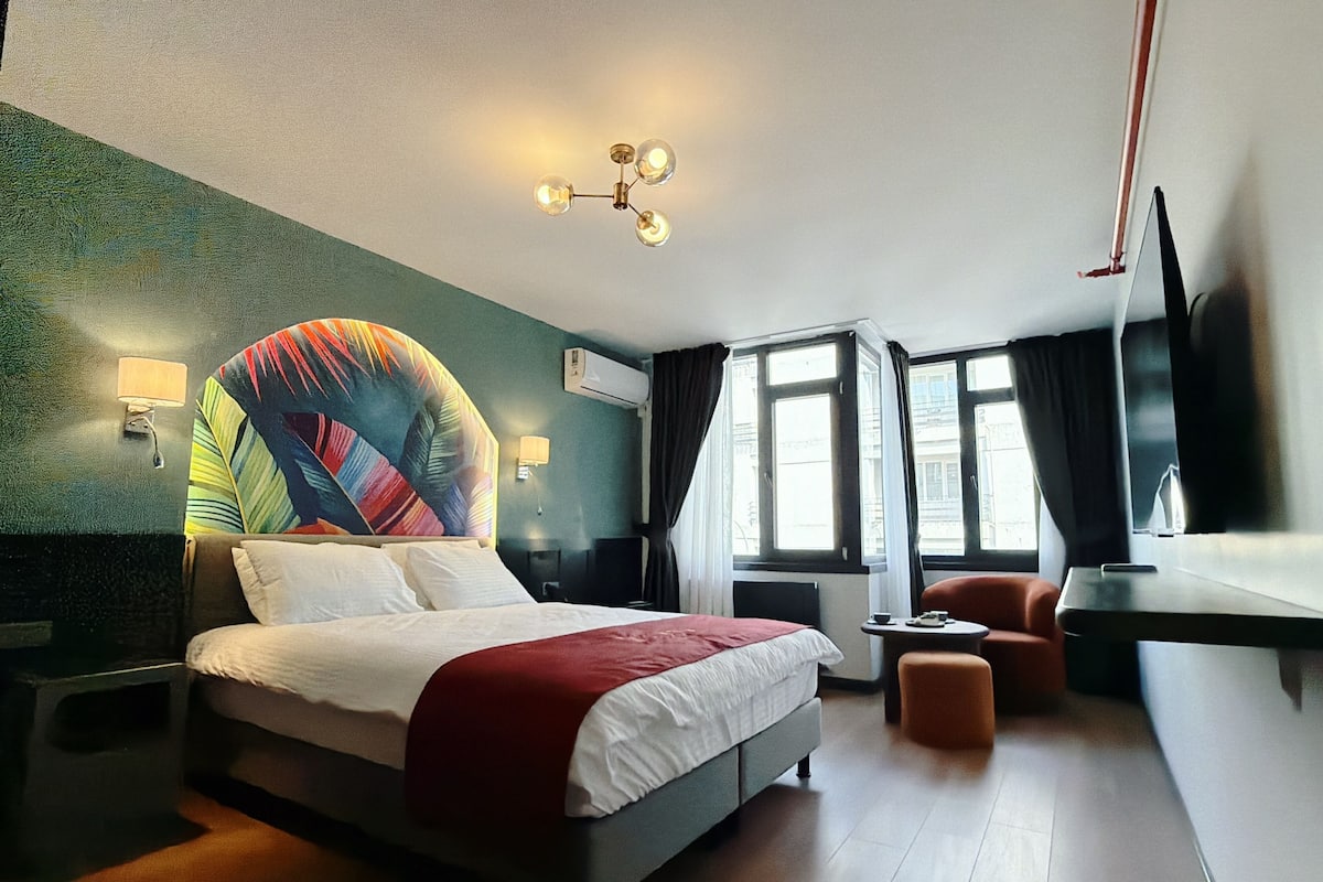 A hotel room with a bed, a desk, a chair, a TV, and a window.