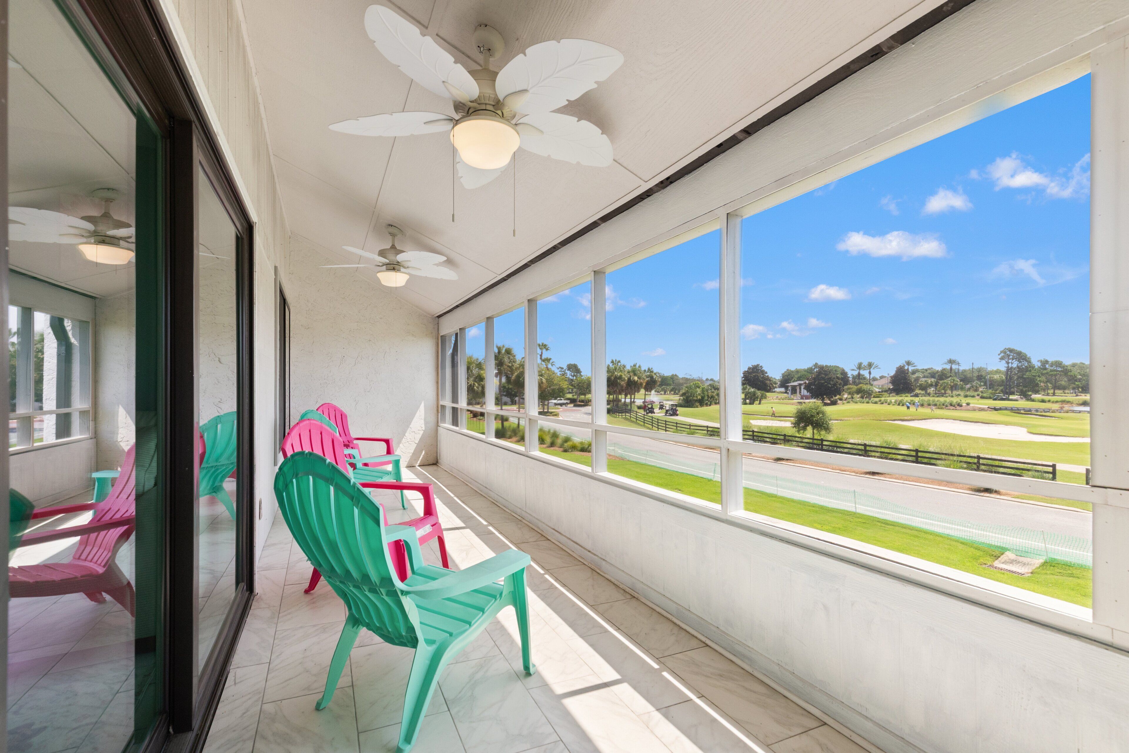 Ein Balkon mit Stühlen, einem Deckenventilator und Blick auf einen Golfplatz.