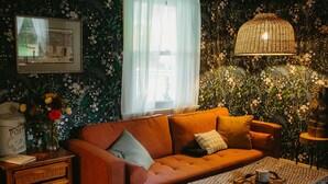Ein gemütliches Wohnzimmer mit einer Couch, Kissen, einem Tisch, einer Lampe und einer Wand mit floralem Wandpapier.
