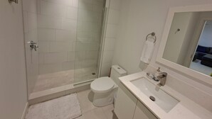 Ett modernt badrum med en duschavdelning med glasväggar, en vit toalett och ett handfat med en spegel ovanför.