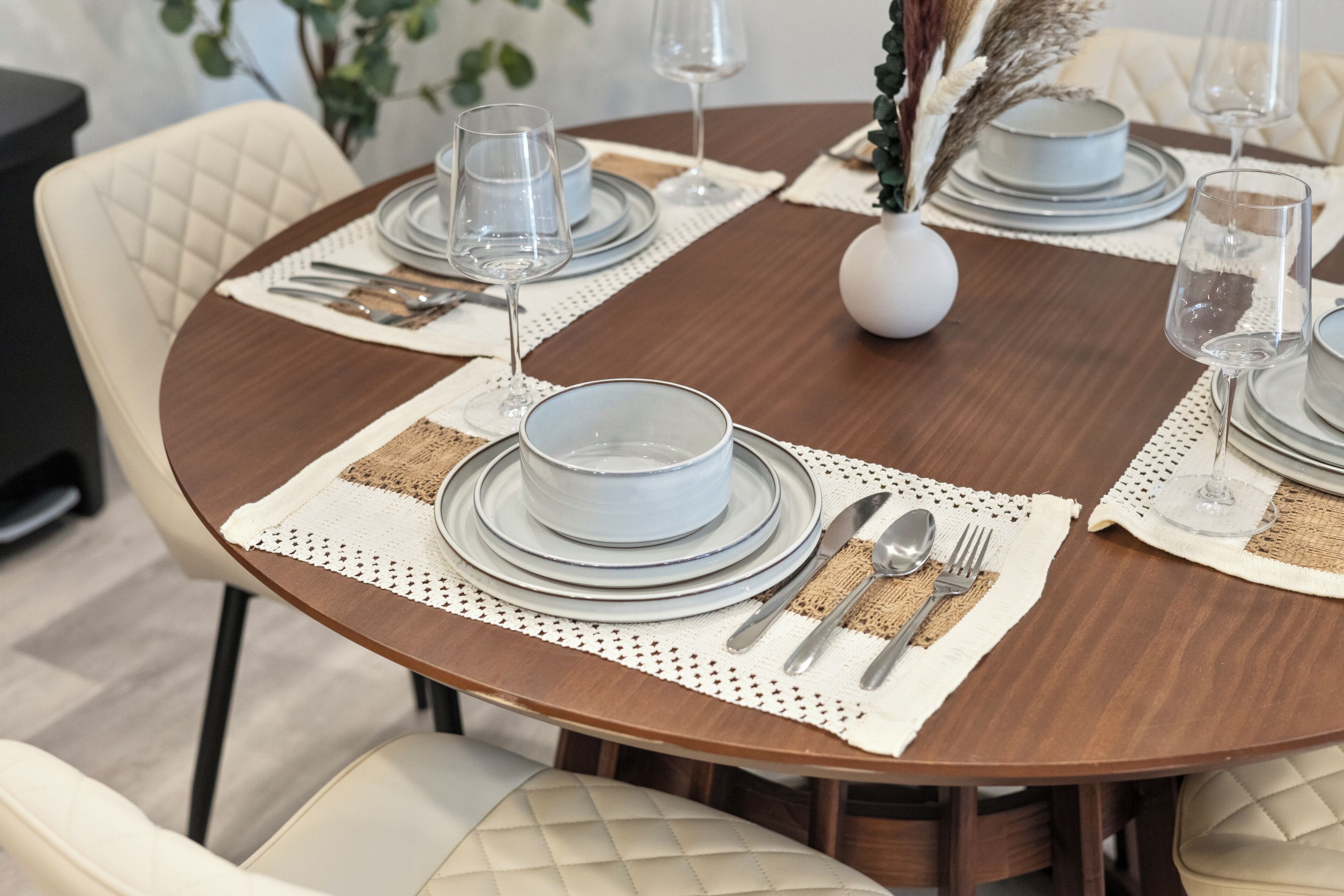 Mesa redonda de comedor con platos blancos, cubiertos y vasos transparentes para cuatro comensales.