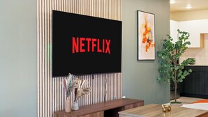 Ett modernt vardagsrum med en platt-TV som är monterad på väggen, en träinredd mediabänk, ett matbord och en krukväxt.
