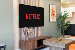 Ein modernes Wohnzimmer mit einem Wand-Fernseher, einer Holz-Unterhaltungseinheit, einem Esstisch und einer Topfpflanze.
