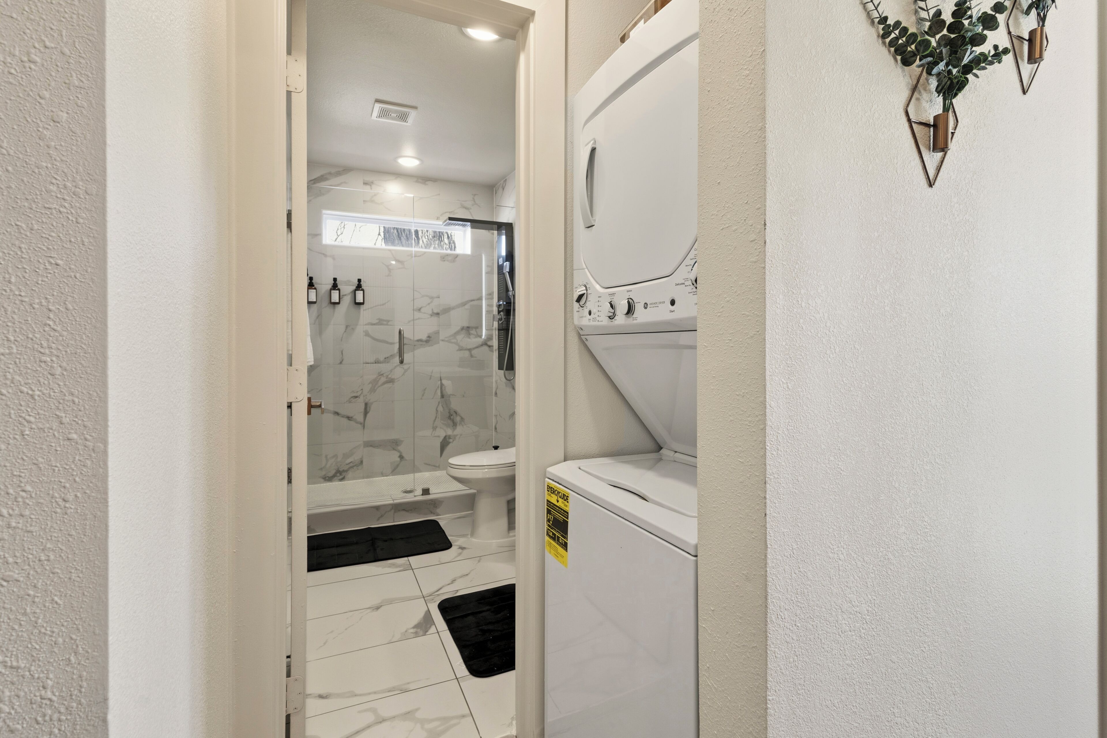 A bathroom with a shower, toilet, and a white washing machine.