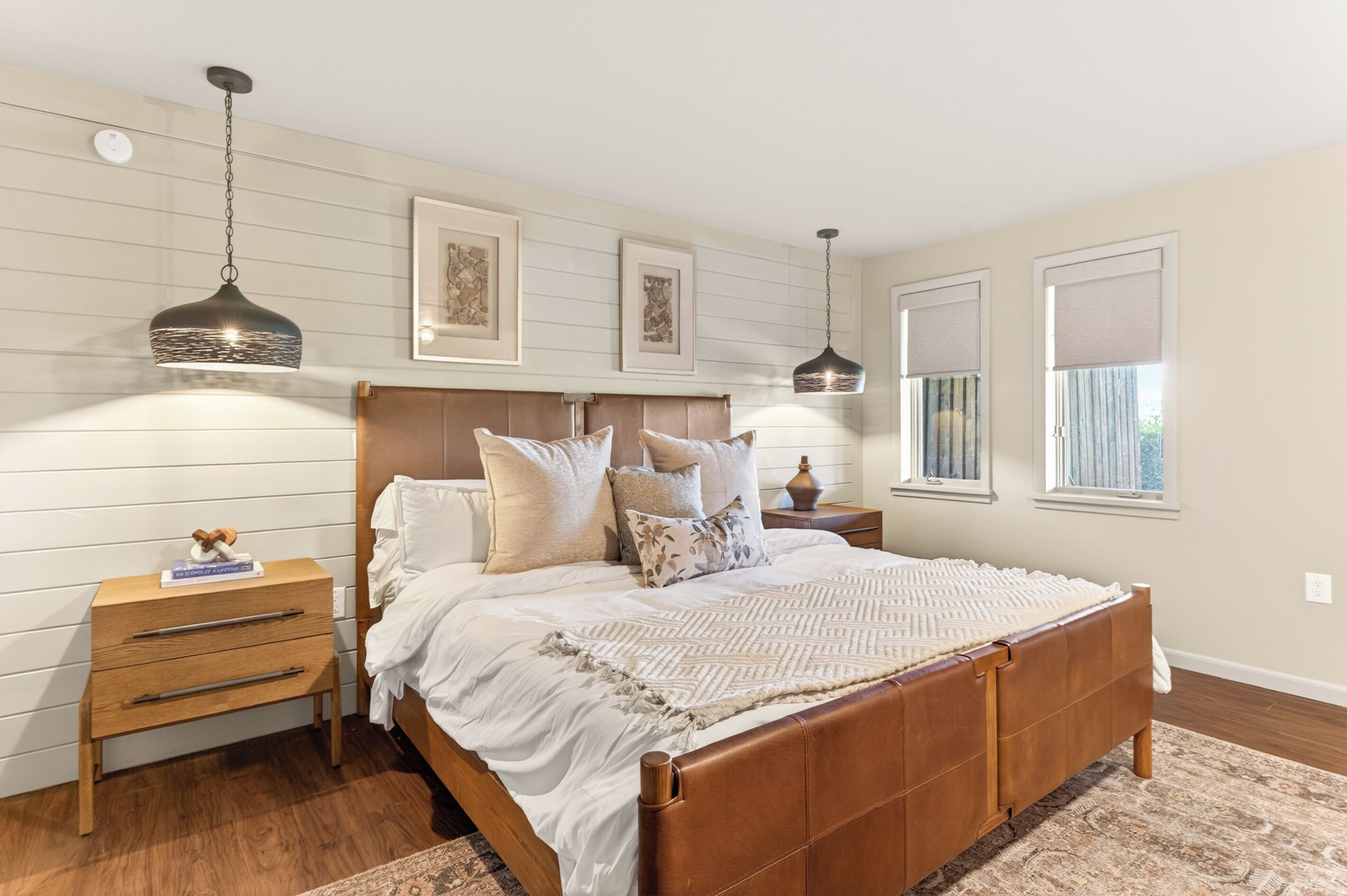 A bedroom with a wooden bed, a nightstand, a lamp, and a window with blinds.