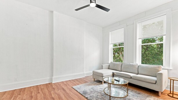 Ein modernes Wohnzimmer mit grauem Sofa, einem Glastisch und einem Deckenventilator.