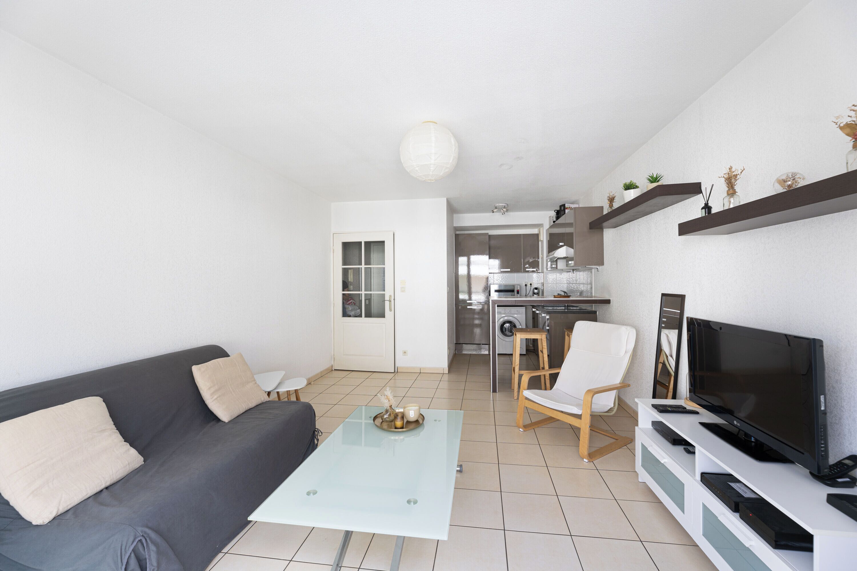 En moderne stue med sofa, sofabord, fjernsyn og et køkken i baggrunden.