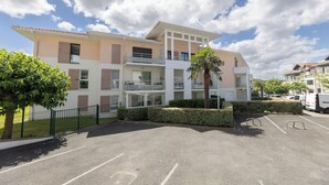 Un immeuble à plusieurs étages avec un parking à l’avant, une clôture verte et un palmier.