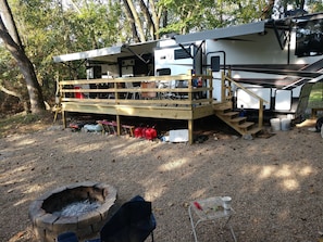 Un veicolo ricreativo con una terrazza coperta, un braciere e un tavolo da barbecue in metallo.