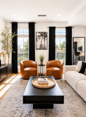 A modern living room with two leather armchairs, a coffee table with books, a framed picture, and a view of the city. - Midnight Luxe Suite with Walkable Areas and Free Parking (Atlanta)