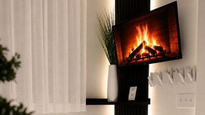 A modern living room with a flat-screen TV mounted on a wall, a fireplace, a white vase with a plant, and a white curtain. - Midnight Luxe Suite with Walkable Areas, Keyless Check-in and Free Parking (Atlanta)