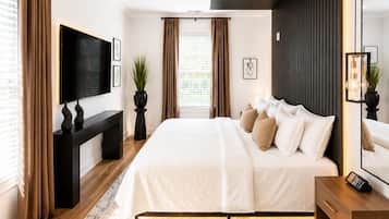 A modern bedroom with a large bed, a TV, a desk, and a mirror.