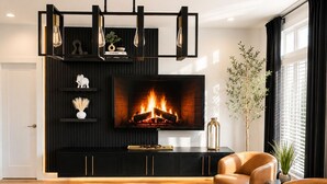 A modern living room with a fireplace, leather chairs, a dining table with placemats, and a black entertainment unit. - Midnight Luxe Suite with Walkable Areas, Keyless Check-in and Free Parking (Atlanta)
