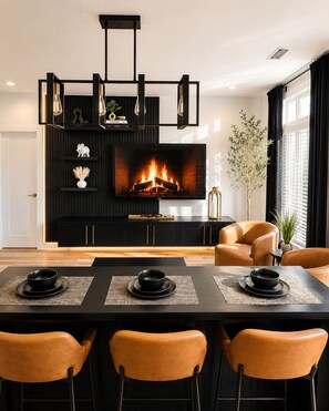 A modern living room with a fireplace, leather chairs, a dining table with placemats, and a black entertainment unit. - Midnight Luxe Suite with Walkable Areas and Free Parking (Atlanta)