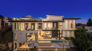 Une maison moderne à plusieurs étages, dotée d’une piscine, d’un espace extérieur aménagé et d’un patio bien éclairé.