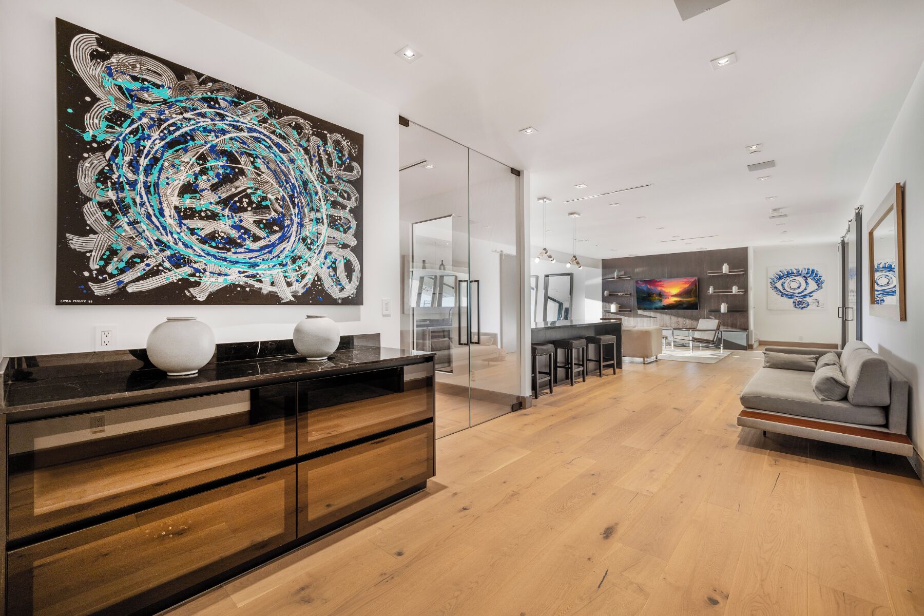 Uma sala de estar moderna com um grande quadro abstrato, uma cozinha ao fundo e uma área de jantar com banquetas de bar.