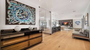 Uma sala de estar moderna com um grande quadro abstrato, uma cozinha ao fundo e uma área de jantar com banquetas de bar.