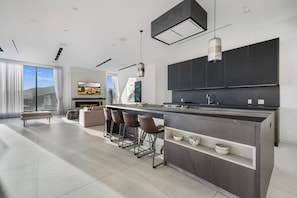 A modern kitchen with a central island, bar stools, and a large TV.