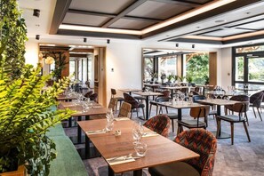 A restaurant with multiple tables, chairs, and potted plants. - Hotel Arcalod - Grand Parc (Doussard)