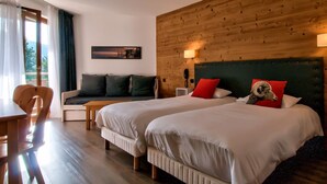 A hotel room with two beds, a wooden headboard, a sofa, a desk, and a phone on the nightstand.