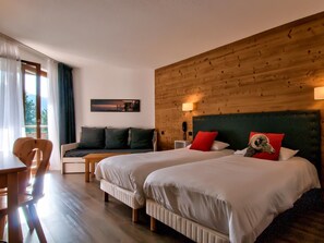Quarto de hotel com duas camas, cabeceira de madeira, sofá, escrivaninha e telefone na mesa de cabeceira.