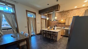 A modern kitchen with a central island, bar stools, a refrigerator, and a brick wall.