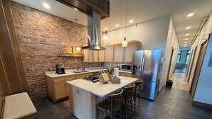 A modern kitchen with a central island, stainless steel appliances, and a brick wall.